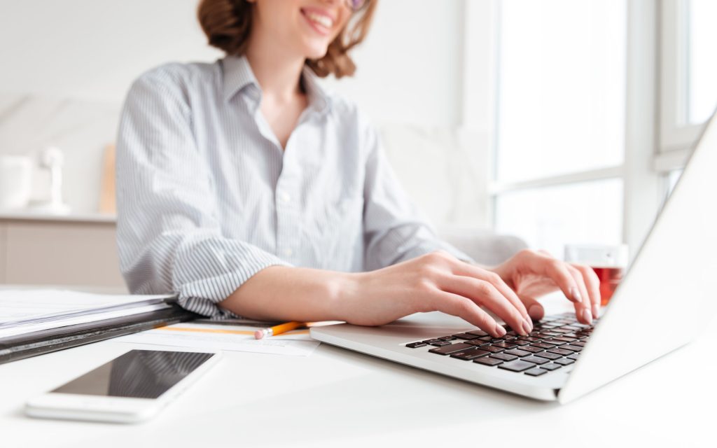 Cropped photo of pretty brunette woman typing email on laptop computer while sitting at home, selective focus on hand